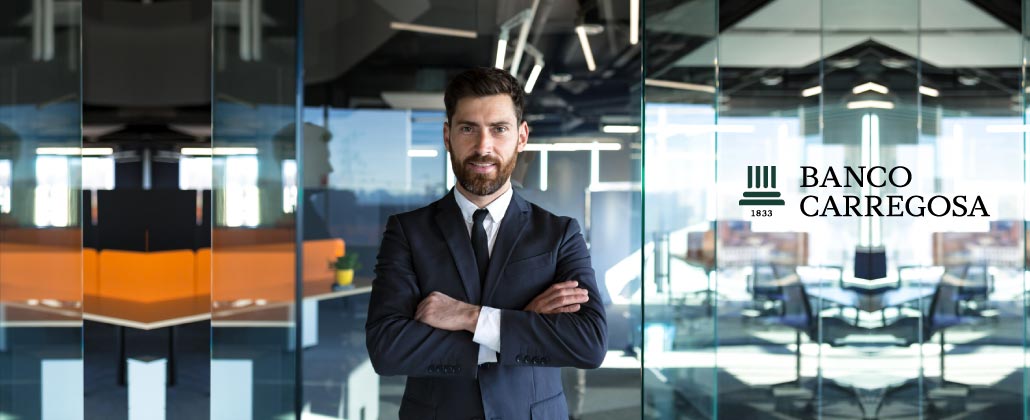 Homem de fato e gravata, de braços cruzados em frente às instalações do Banco Carregosa.